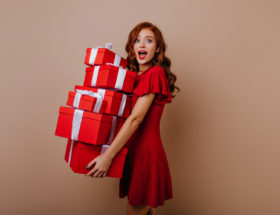 mulher em um vestido vermelho carregando caixas de presentes