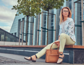 Mulher sentada em um banco na rua segurando uma bolsa marrom