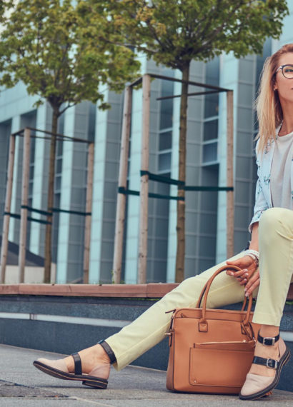 Mulher sentada em um banco na rua segurando uma bolsa marrom