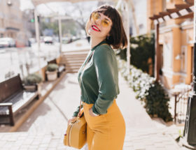 Mulher posando na rua com uma bolsa amarela de couro a tiracolo