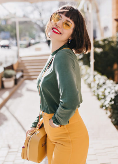 Mulher posando na rua com uma bolsa amarela de couro a tiracolo